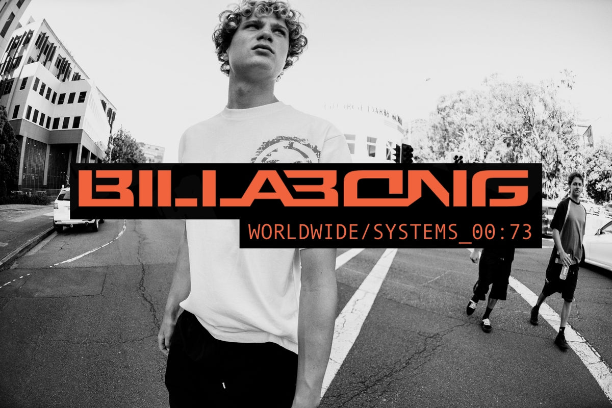 A black and white street scene with a young man in the foreground wearing a white t-shirt and dark pants, with a large Billabong logo overlay across the center reading 'BILLABONG' and 'WORLDWIDE/SYSTEMS_00:73'.