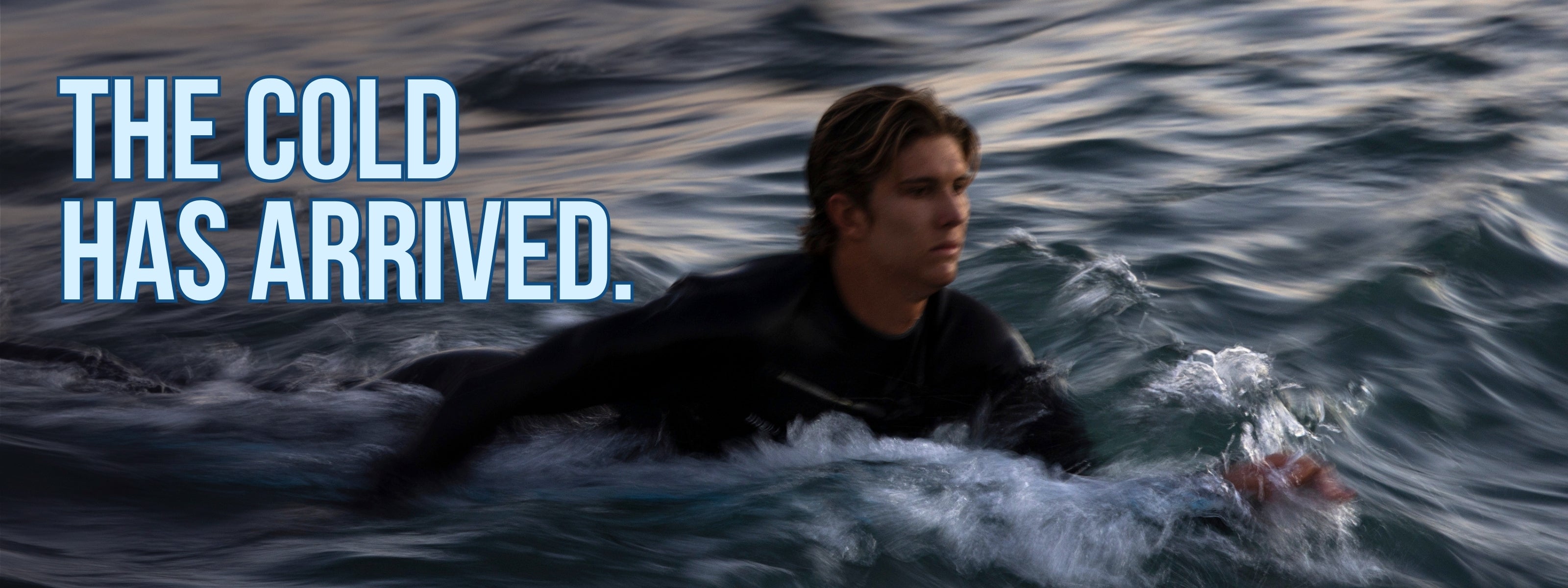 Person in a wetsuit swimming in cold water with text 'THE COLD HAS ARRIVED.'
