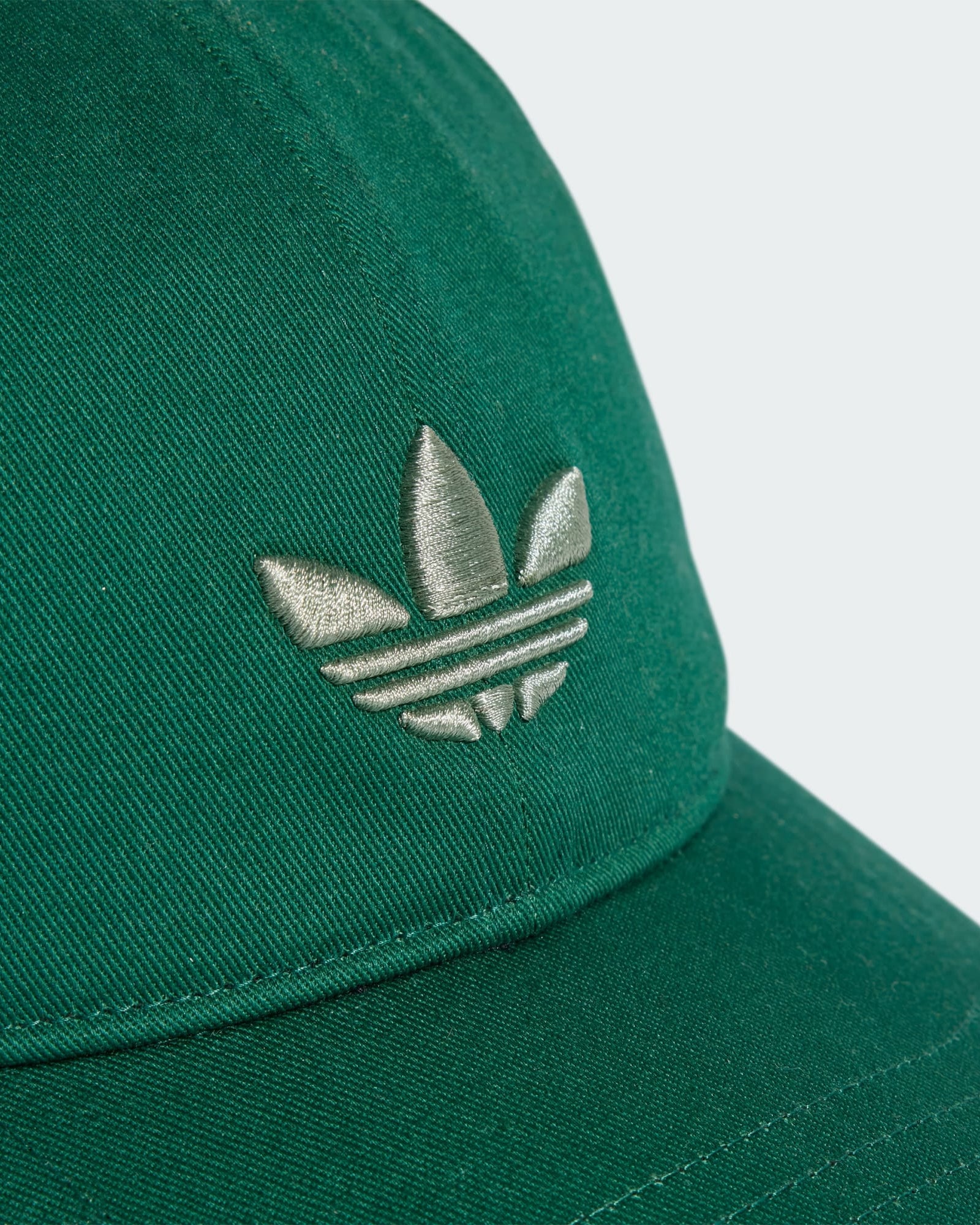 Close-up of a green Adidas cap featuring an embroidered metallic silver Trefoil logo on the front panel with stitched details