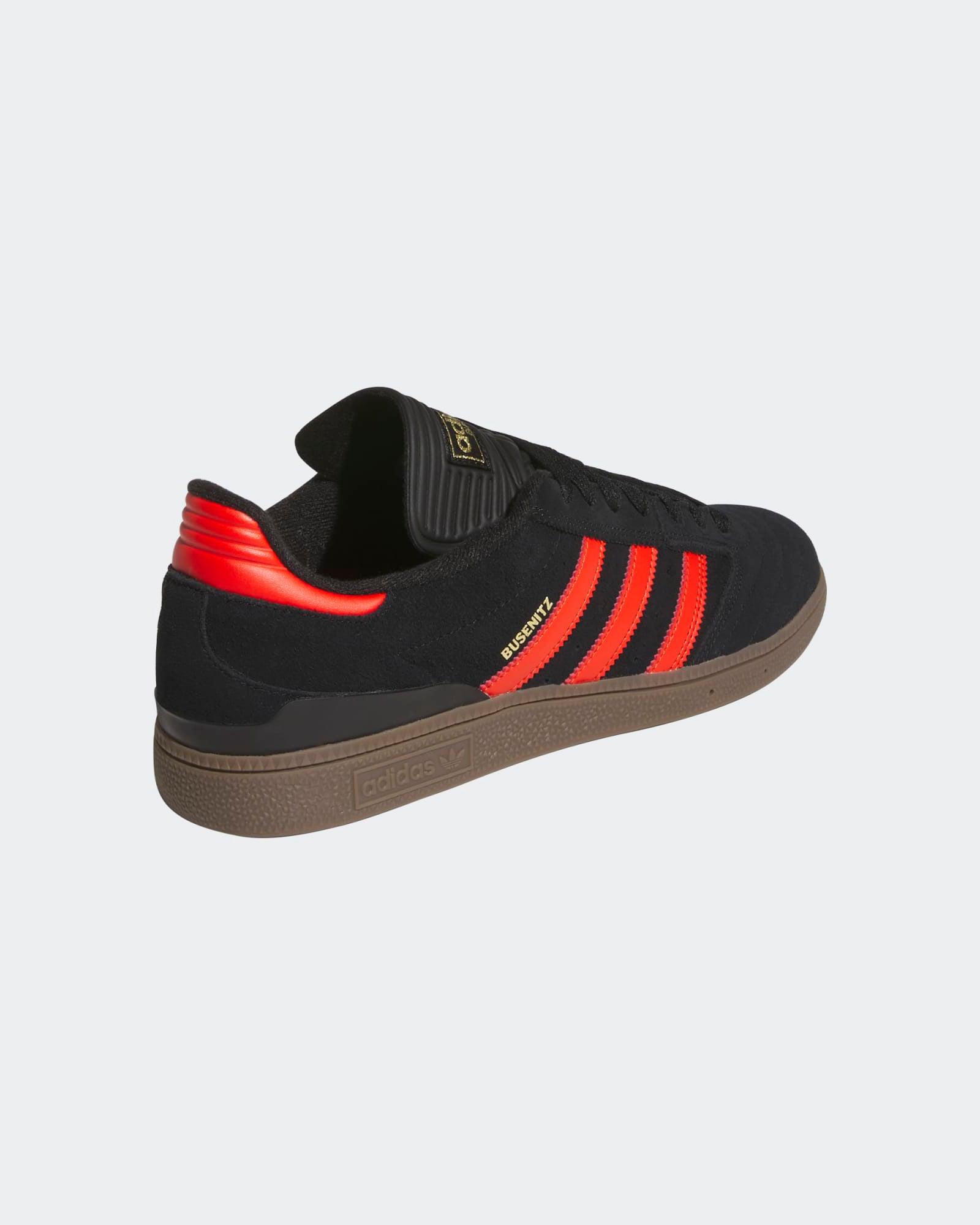 Angled view of black Adidas sneakers with vibrant red stripes, gold branding, a gum sole, and a sleek, modern design.
