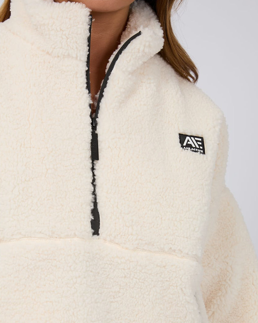 Close-up of a cream sherpa fleece pullover featuring a half-zip front with black trim and a black AAE Active logo patch.