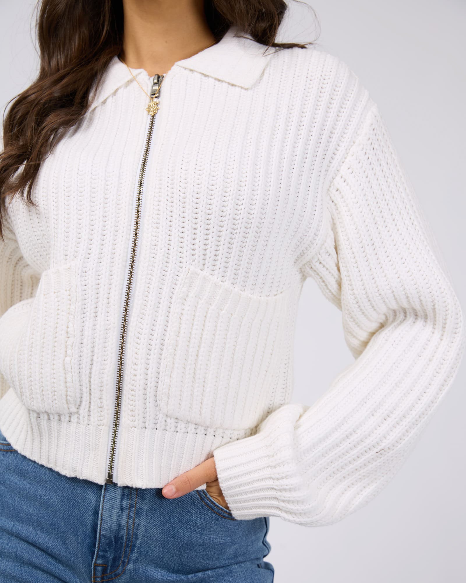 Close-up of a model wearing a white ribbed knit zip-up cardigan with a collar, front pockets, and balloon sleeves.