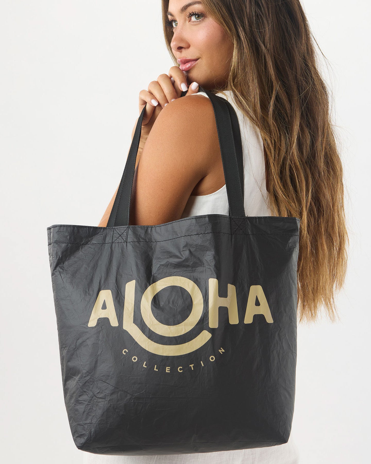 Woman holding reversible black tote bag with large beige ALOHA Collection logo