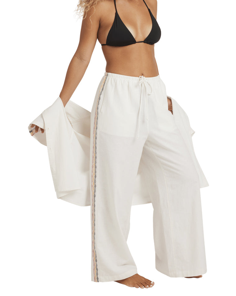 Side view of white embroidered pants with drawstring waist, paired with black bikini top and open shirt.