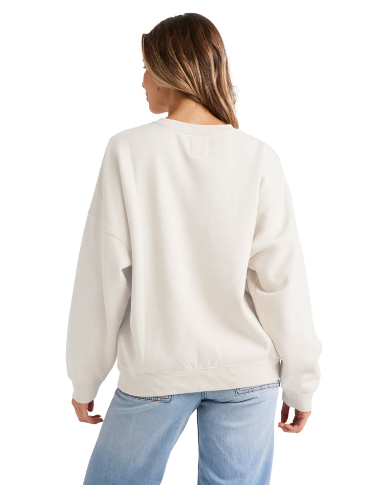 Model wearing a cream oversized Billabong sweatshirt from the back, paired with light blue jeans.