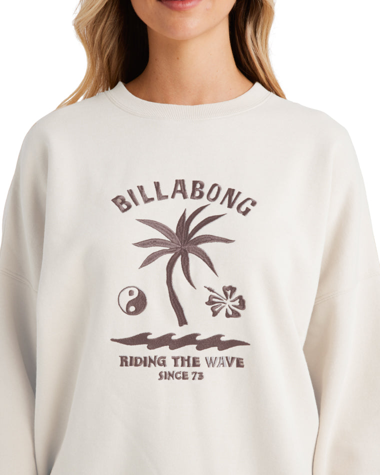 lose-up of a cream Billabong sweatshirt featuring a brown embroidered tropical graphic with a palm tree and waves.