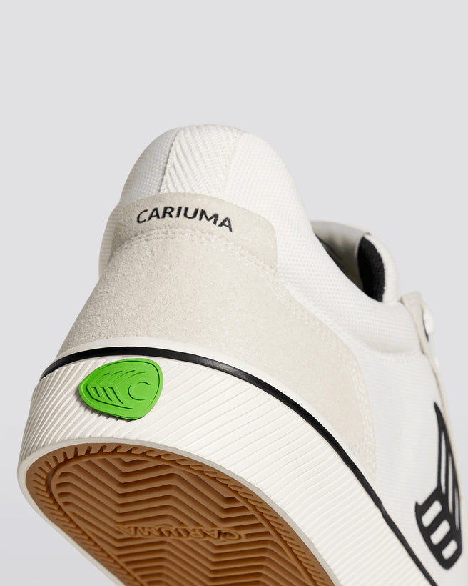 Close-up of white Cariuma Vallely sneaker heel, featuring suede detail, black branding, and green leaf logo on the sole.
