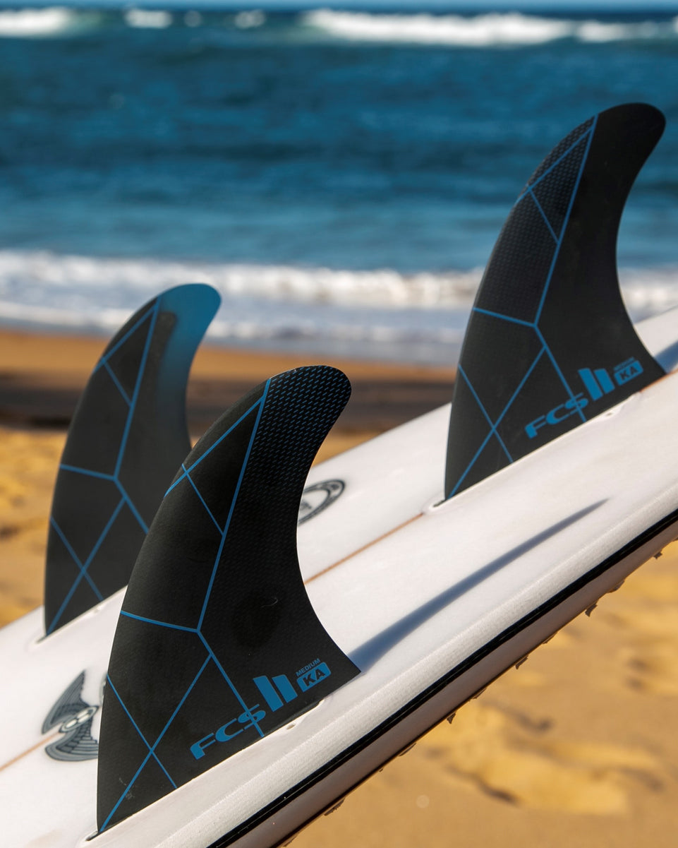 FCS II KA Medium fins installed on surfboard, displayed on sand near the shoreline