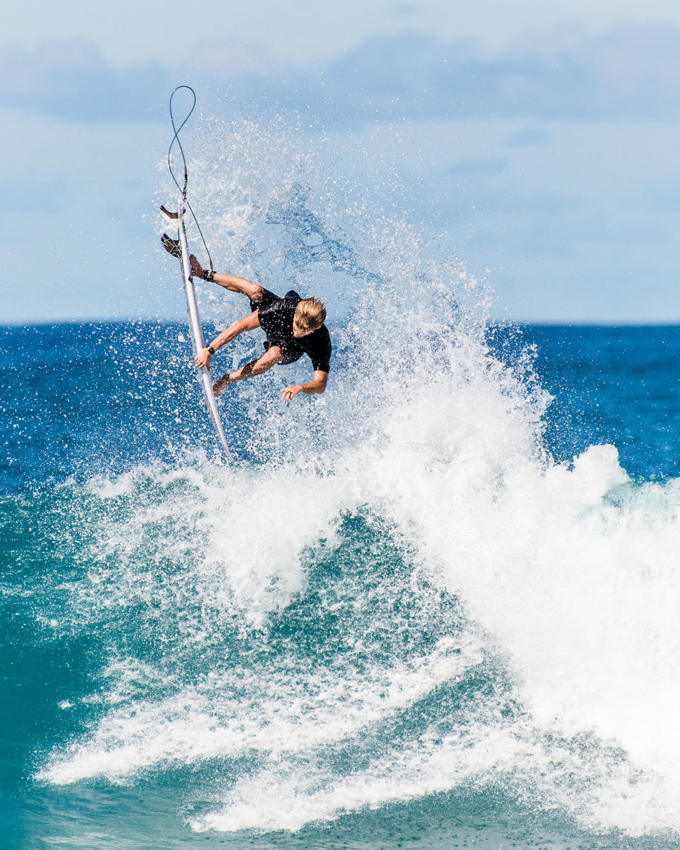 Surfer performing aerial manoeuvre with FCS II KA fins in white surf above turquoise water