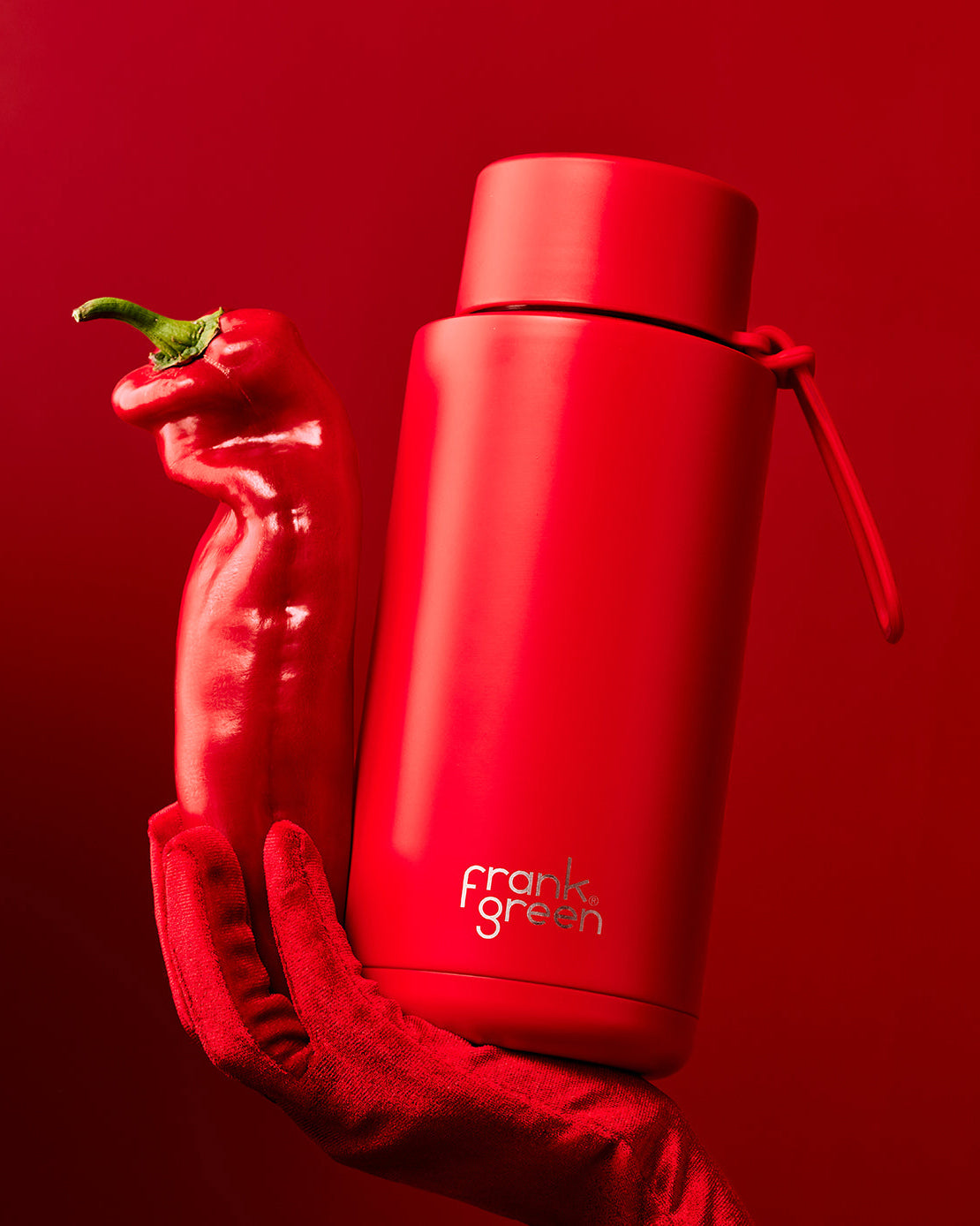 Vibrant red Frank Green water bottle with a sleek design, styled alongside a red chili pepper for a bold lifestyle aesthetic.