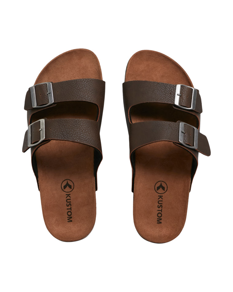 Top-down view of a pair of brown double-strap sandals with metallic buckles, brown footbeds, and "Kustom" branding visible on the insoles.