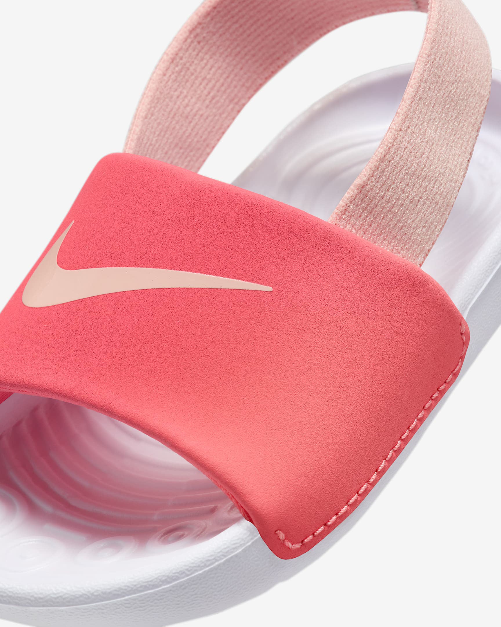 Close-up of pink Nike sandal strap with white Swoosh logo and textured white footbed.