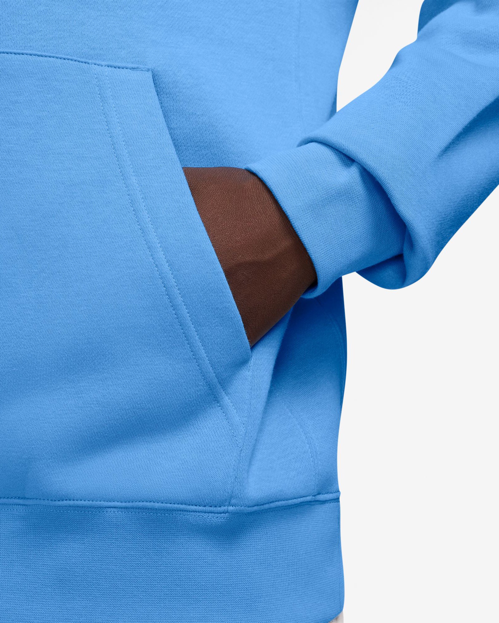 Close-up of a model's hand inside the kangaroo pocket of a bright blue Nike hoodie, showing soft fabric and stitching details.