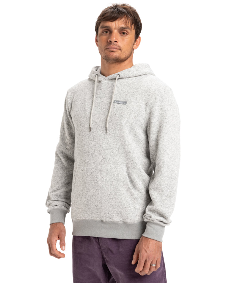 Man wearing a light gray hoodie with drawstrings and a small logo on the chest, paired with purple pants.