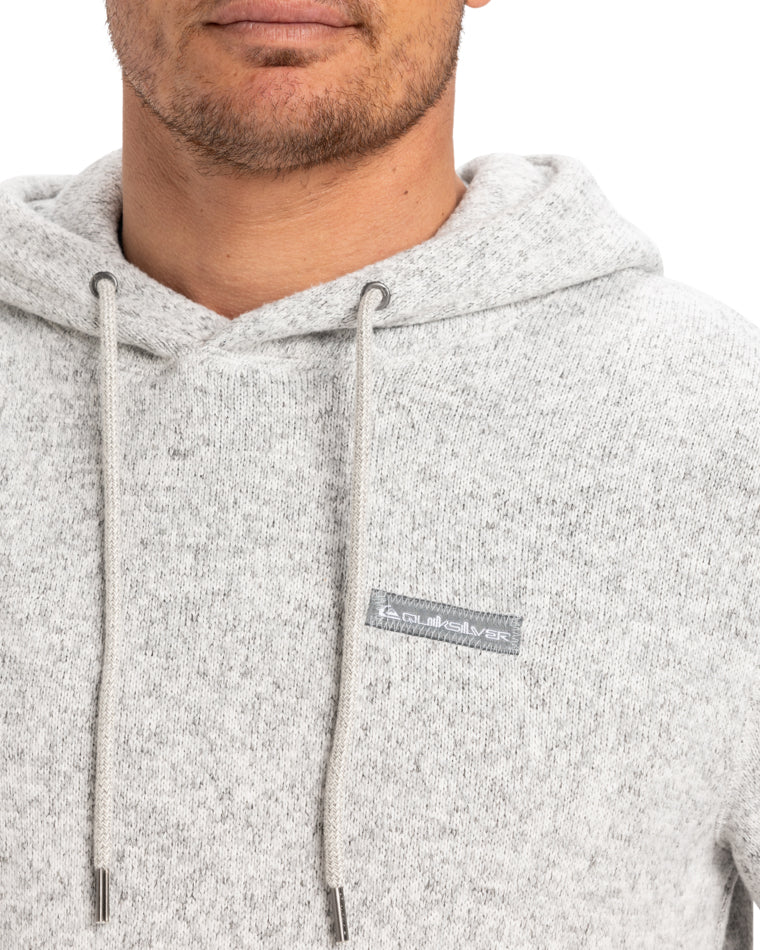 Close-up of a light gray hoodie with drawstrings and a small Quiksilver logo patch on the chest.