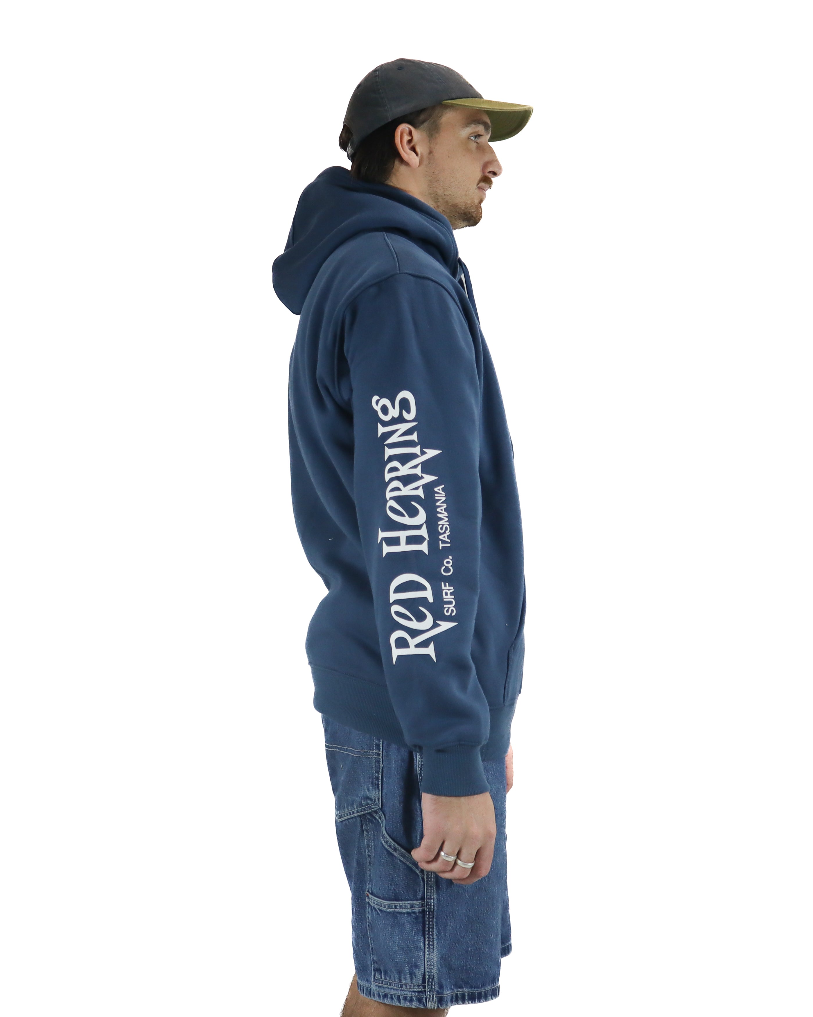 Side view of a blue hoodie with Red Herring Surf Co. Tasmania graphic down the sleeve, styled with denim cargo shorts.