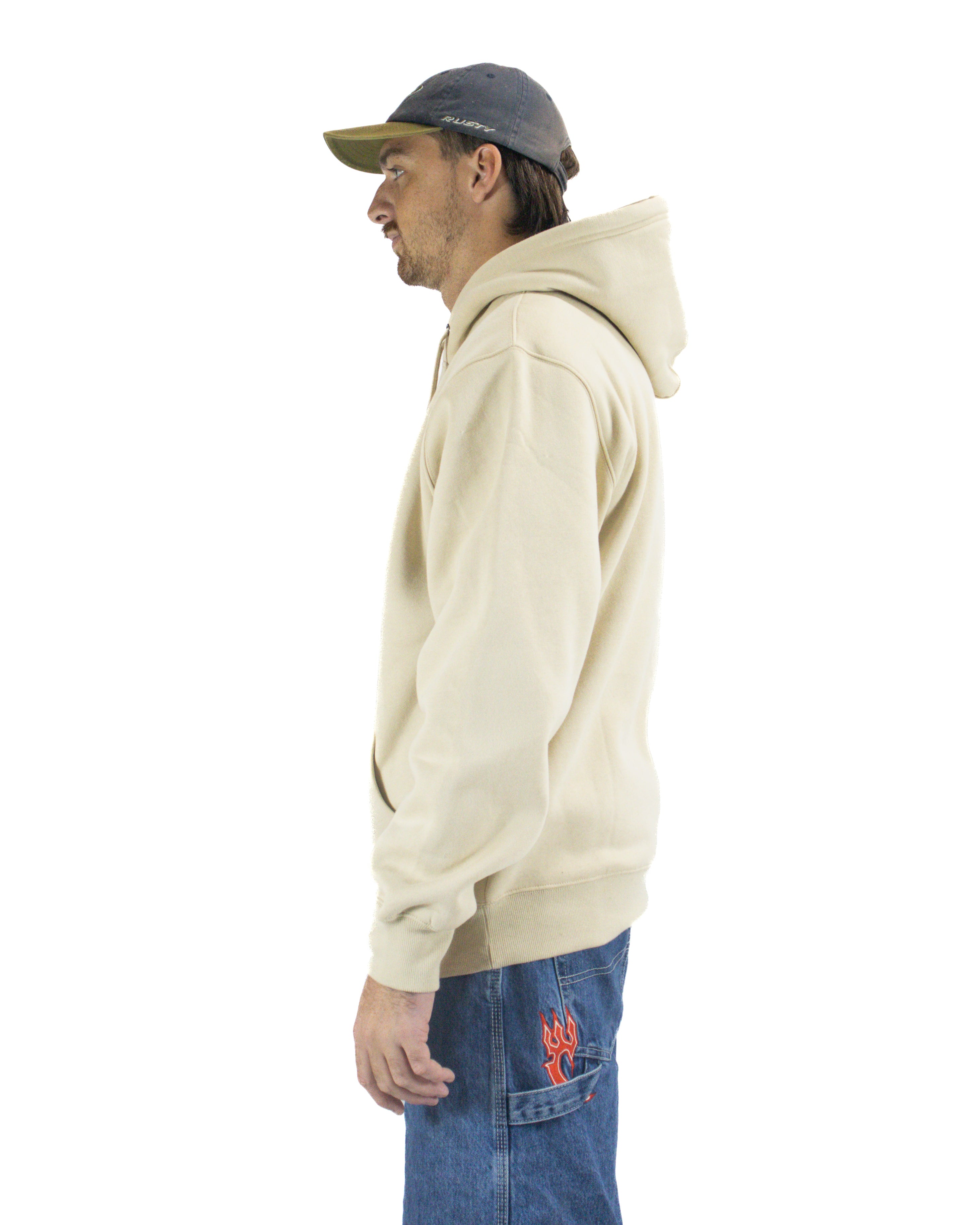 Left side view of a man in a beige hoodie, denim cargo jeans with flame detail, and a grey cap.