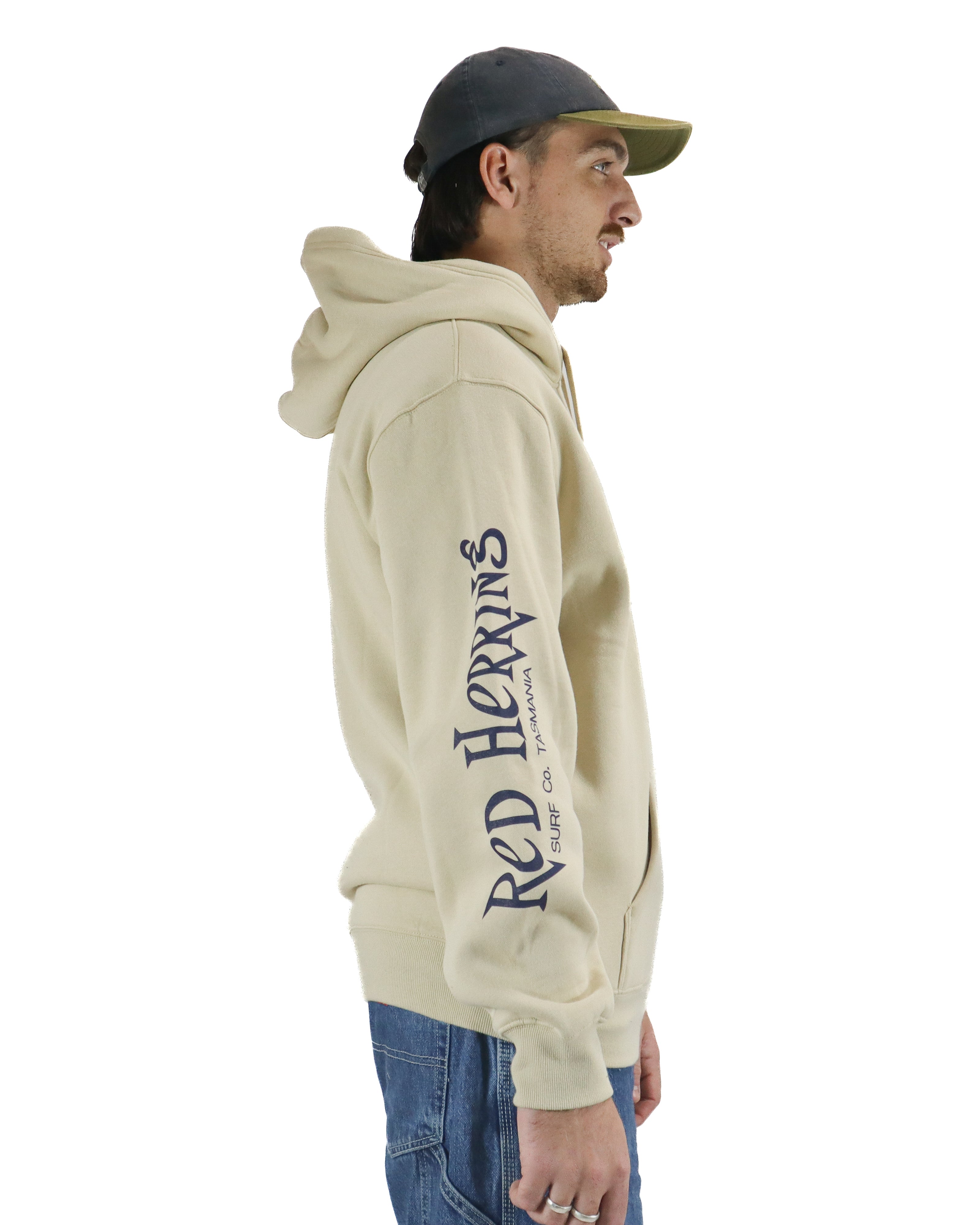 Right side view of a beige hoodie with Red Herring Surf Co. Tasmania text on sleeve, worn with cargo jeans and cap.