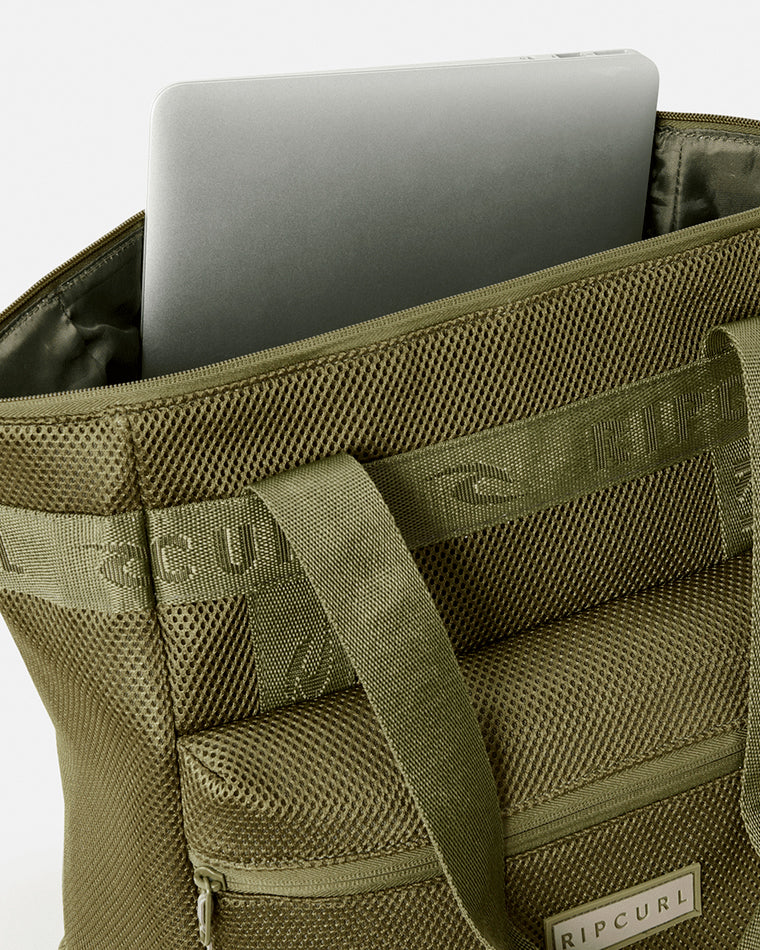 Olive green Rip Curl tote bag with mesh panels, branded handles, and a laptop partially inserted into the main compartment.