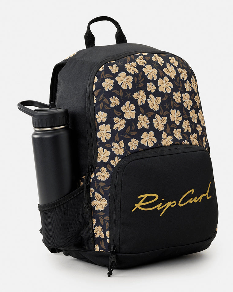 Black Rip Curl backpack with beige floral pattern, front zippered pocket, mesh side pocket holding a black water bottle, and handle.