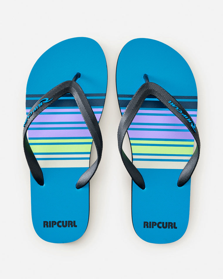 Top-down view of blue Rip Curl thongs with neon green, purple, and white stripes