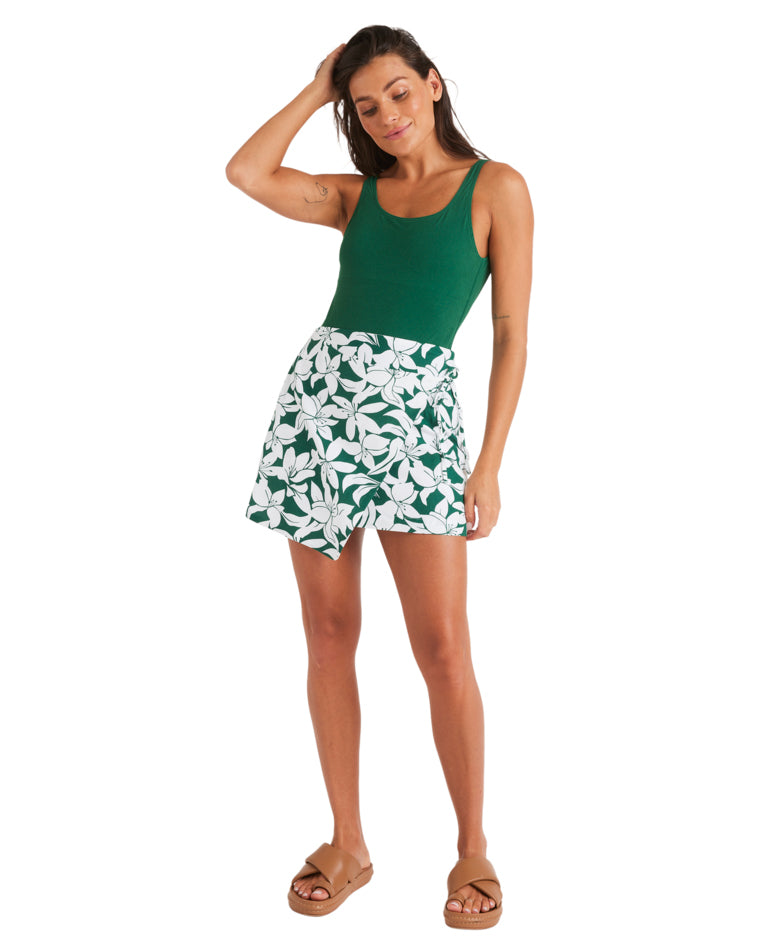 Full body view of woman wearing green bodysuit, floral wrap skirt and tan slide sandals.