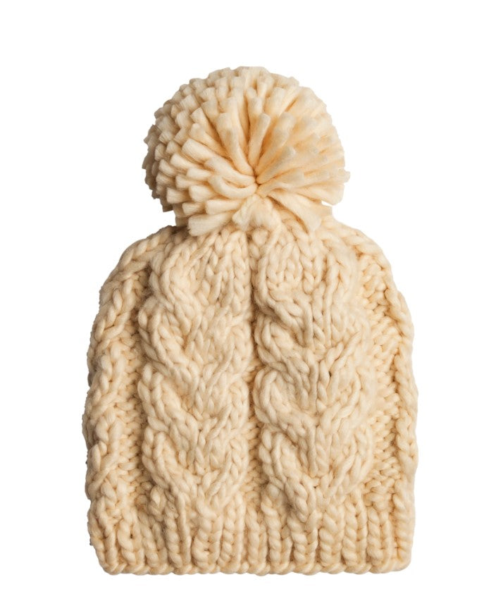 Cream-colored chunky knit beanie with a cable pattern and a fluffy pom-pom on top, displayed against a white background.