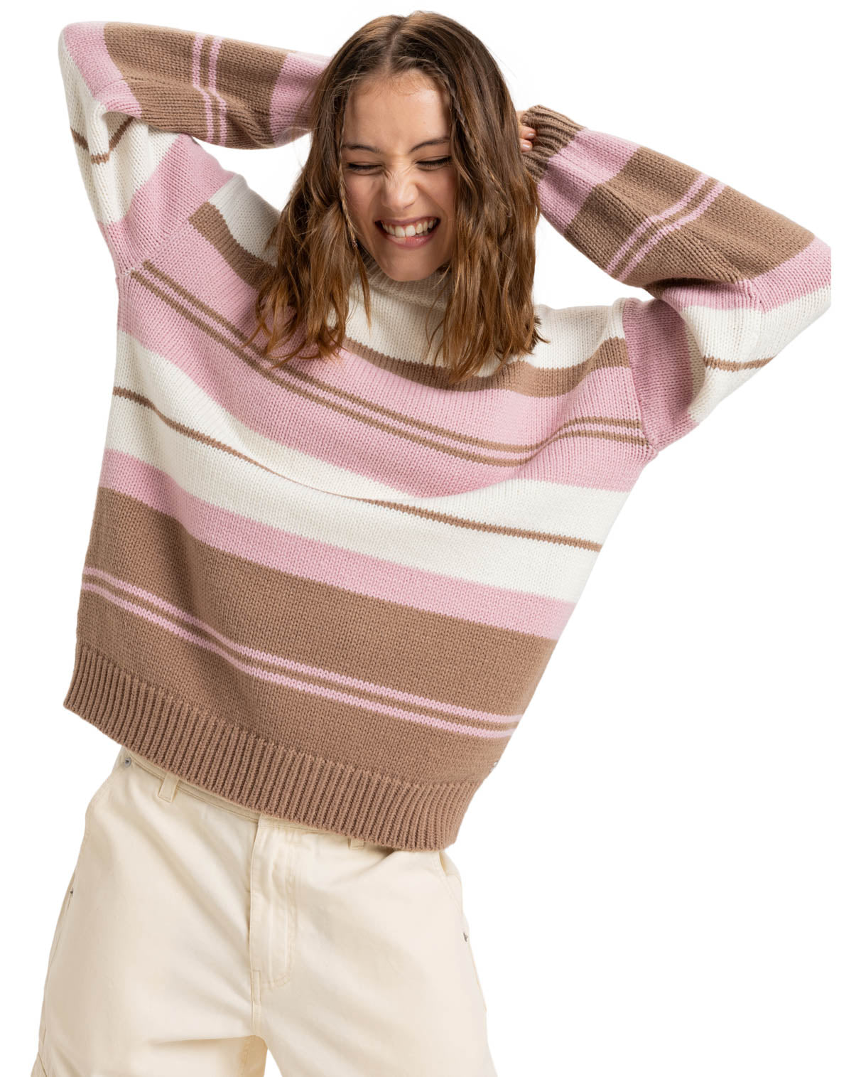 Model wearing a cozy oversized striped sweater in shades of pink, white, and brown, paired with beige pants, smiling.