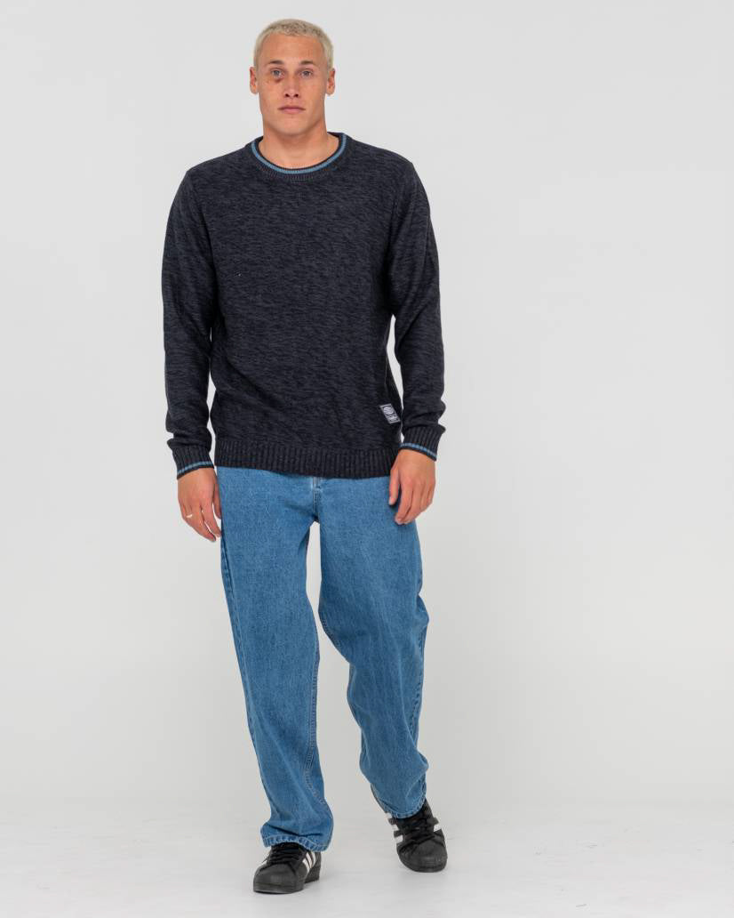 Male model wearing a dark navy knit sweater with ribbed cuffs and hem, paired with blue jeans and black Adidas sneakers.