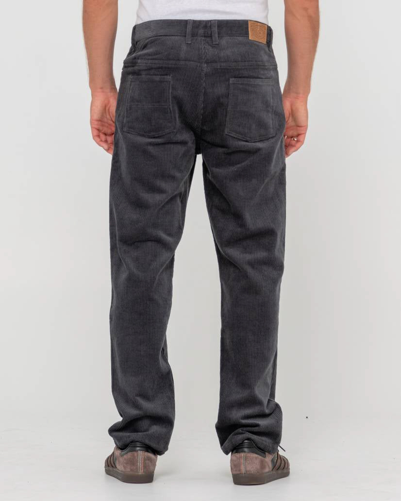Back view of a man wearing dark grey corduroy pants with two back pockets, a leather patch, and worn-out sneakers.