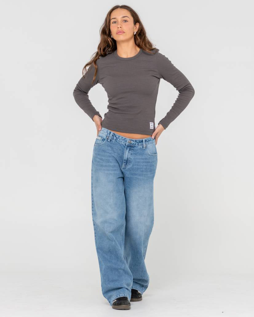 Model wearing a fitted dark grey long-sleeve top and light blue oversized wide-leg jeans, posing with hands on hips.