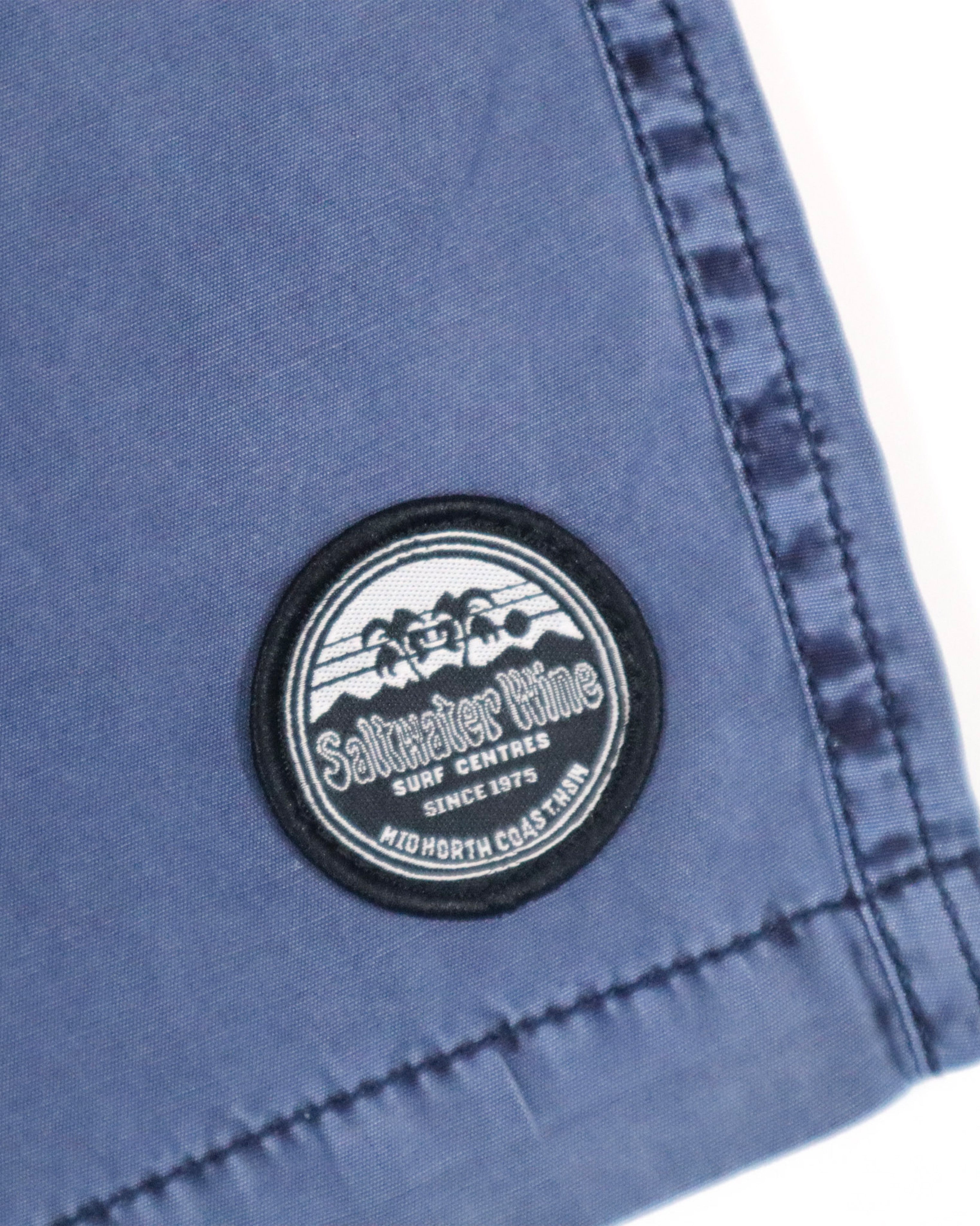 Close-up of circular Saltwater Wine Surf Centres logo patch on the left leg hem