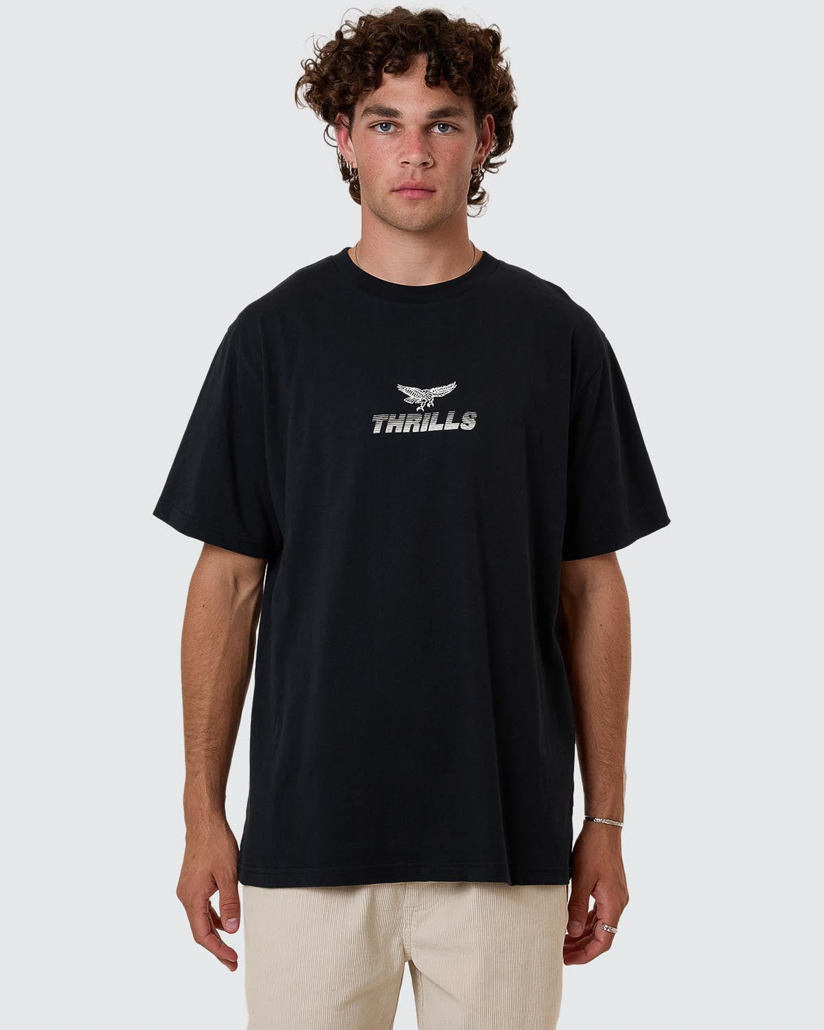 Model wearing black Thrills t-shirt with eagle logo and text graphic on chest, short sleeves and crew neck