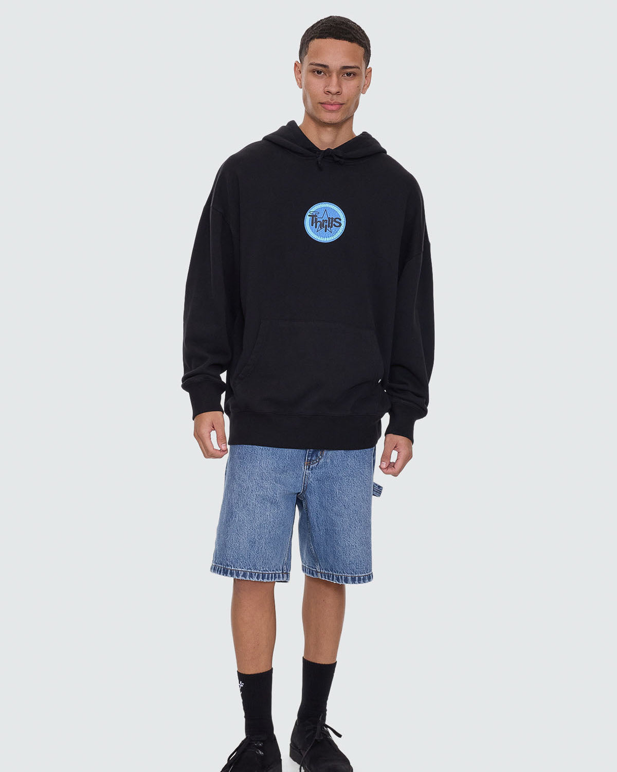 Black hoodie with blue Thrills chest logo, styled with blue denim shorts.