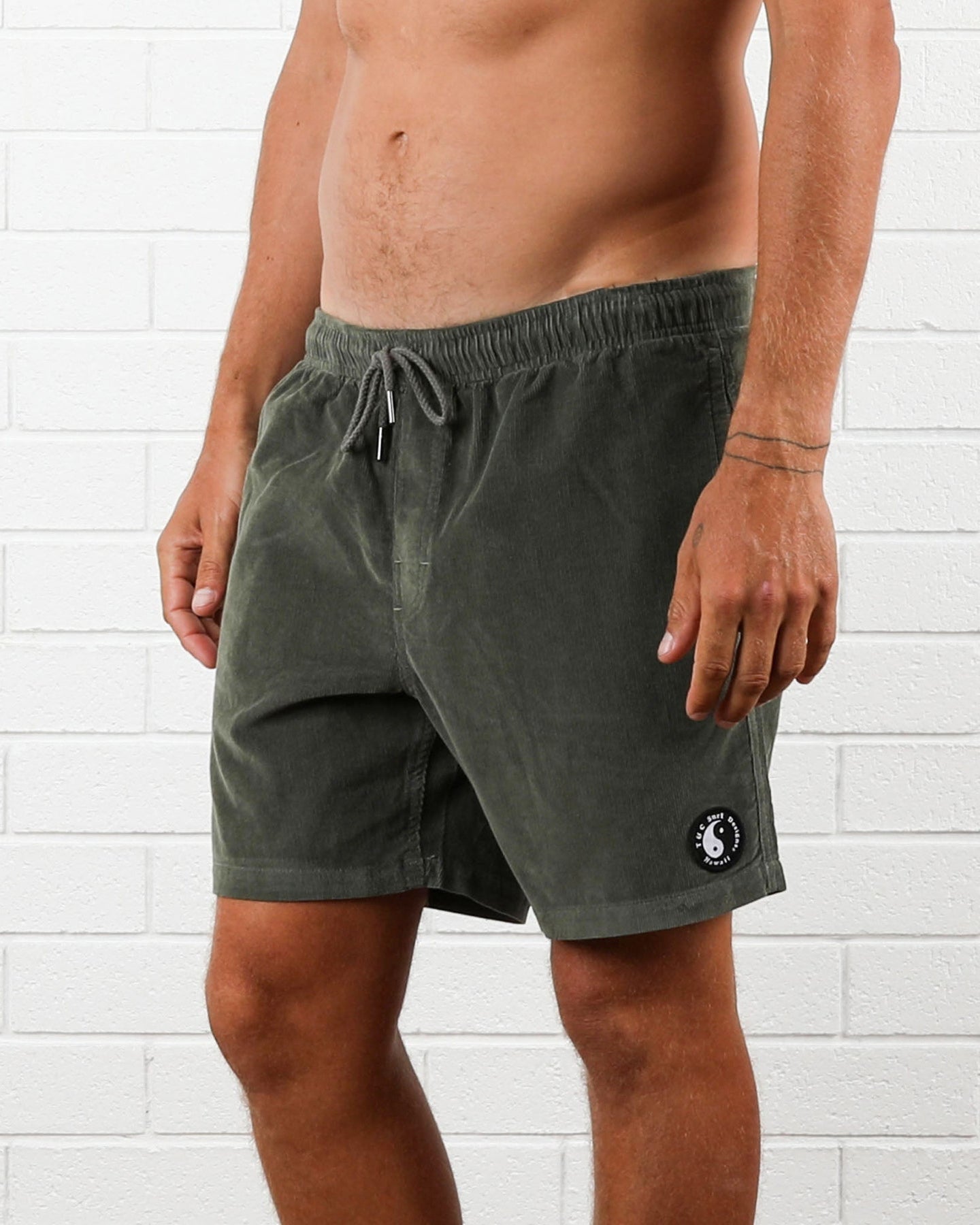 Side view of olive cord shorts featuring logo patch near hem