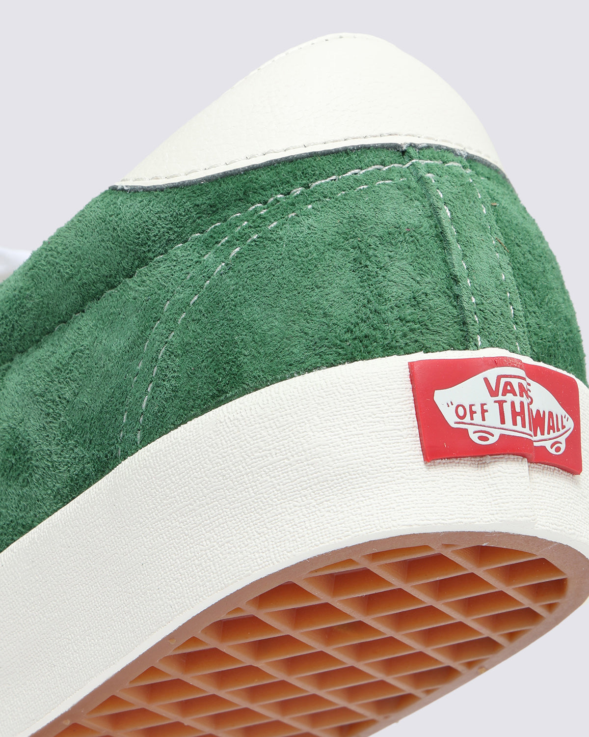Close-up of green suede Vans sneaker heel with white leather accent, red 'Off The Wall' logo, and waffle-patterned sole.