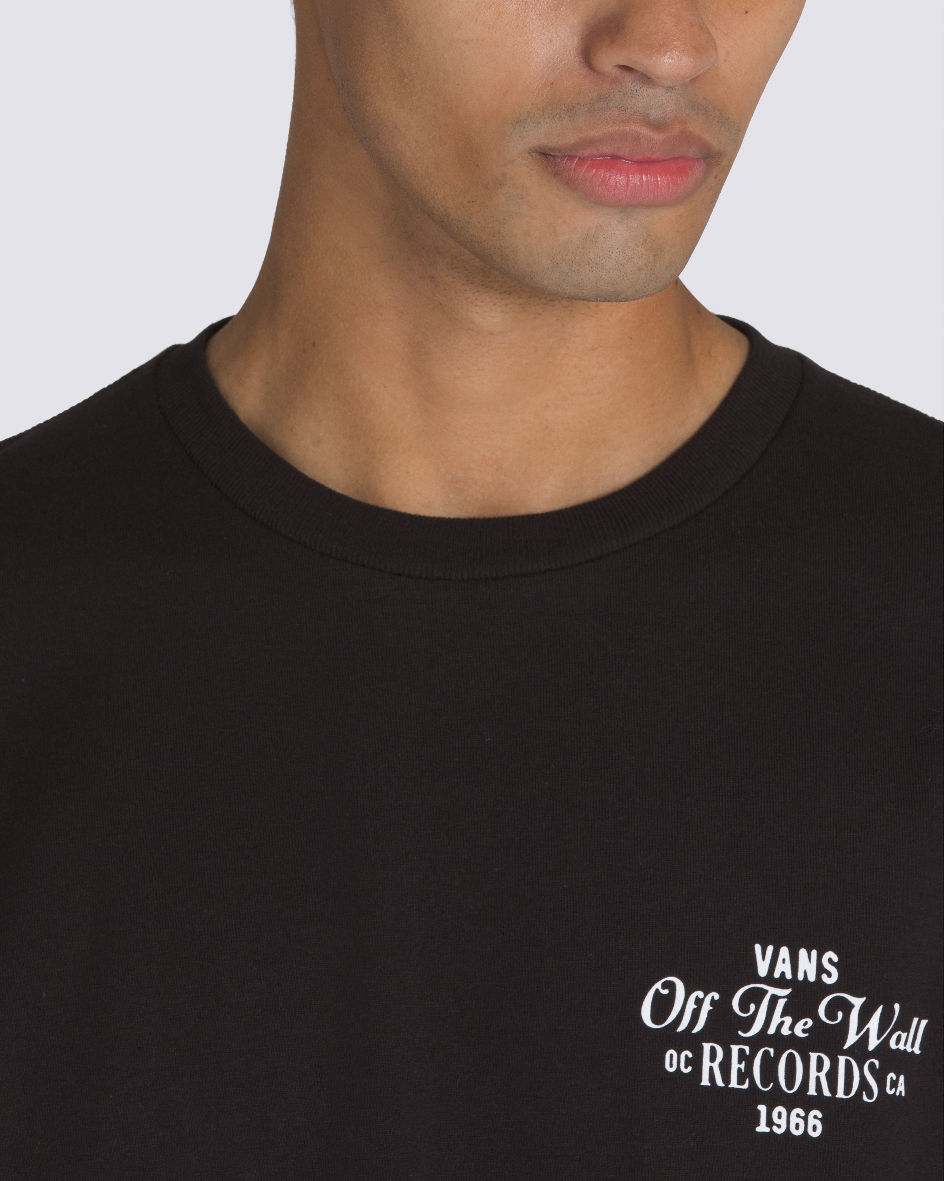 Close-up of a black Vans Off The Wall Records t-shirt with white text logo on the chest, worn by a model.