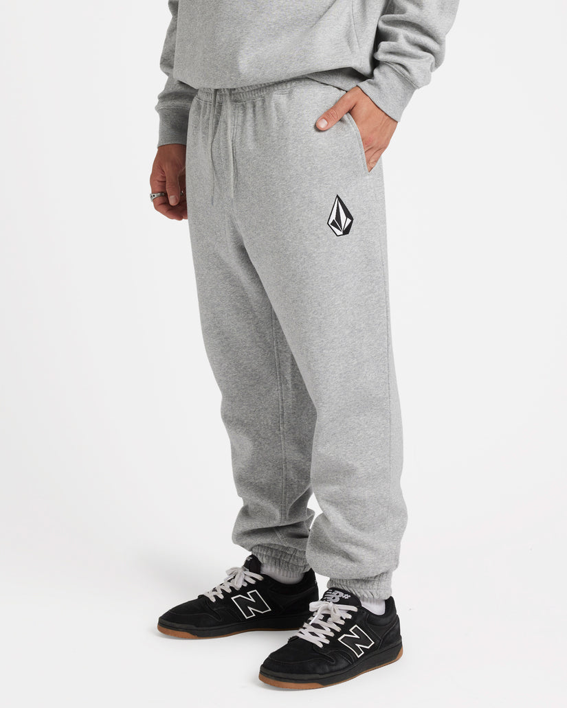 Side view of model wearing light grey sweatpants with a black Volcom logo on the thigh, elastic cuffs, and black sneakers.