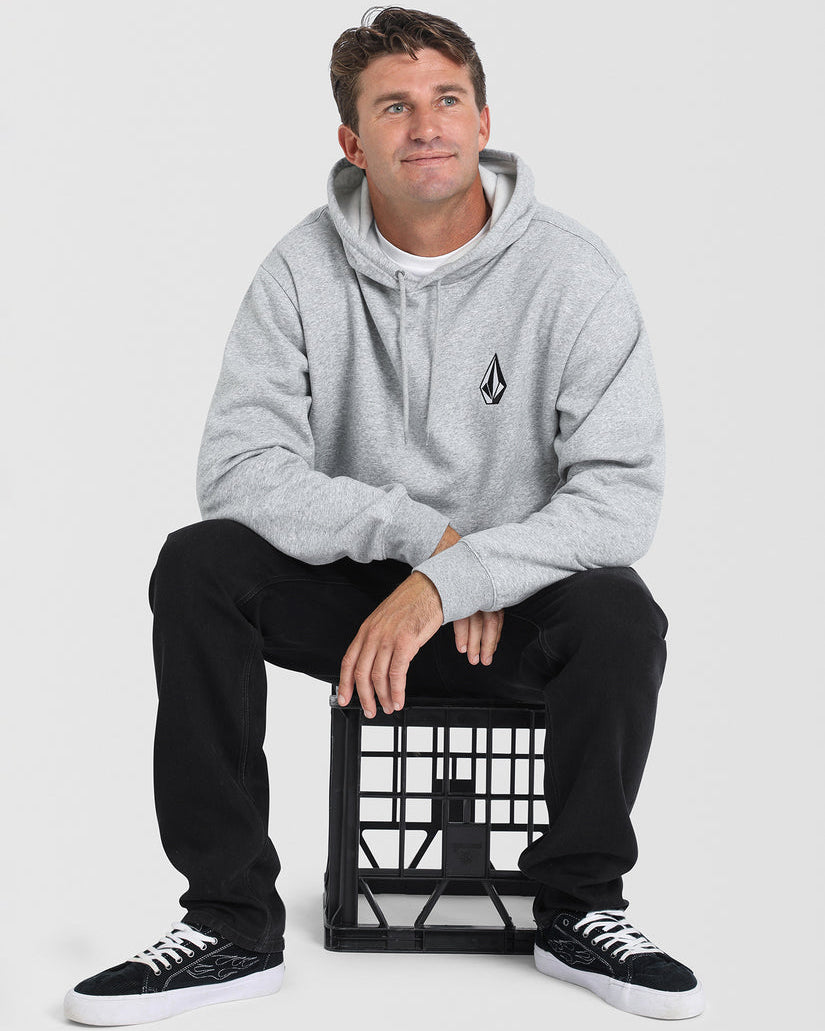 Male model sitting on a black crate, wearing a grey Volcom hoodie with a black logo, black pants, and black sneakers with white soles.