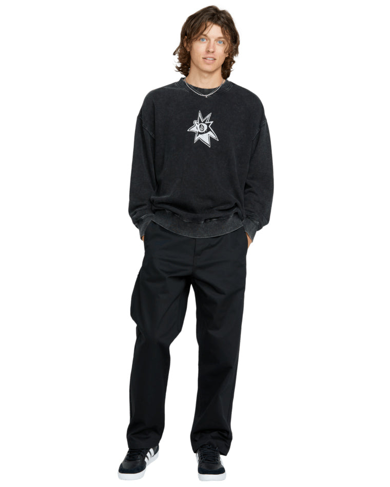 Male model wearing a black vintage-wash Volcom crewneck sweatshirt with a distressed logo, black pants, and sneakers.
