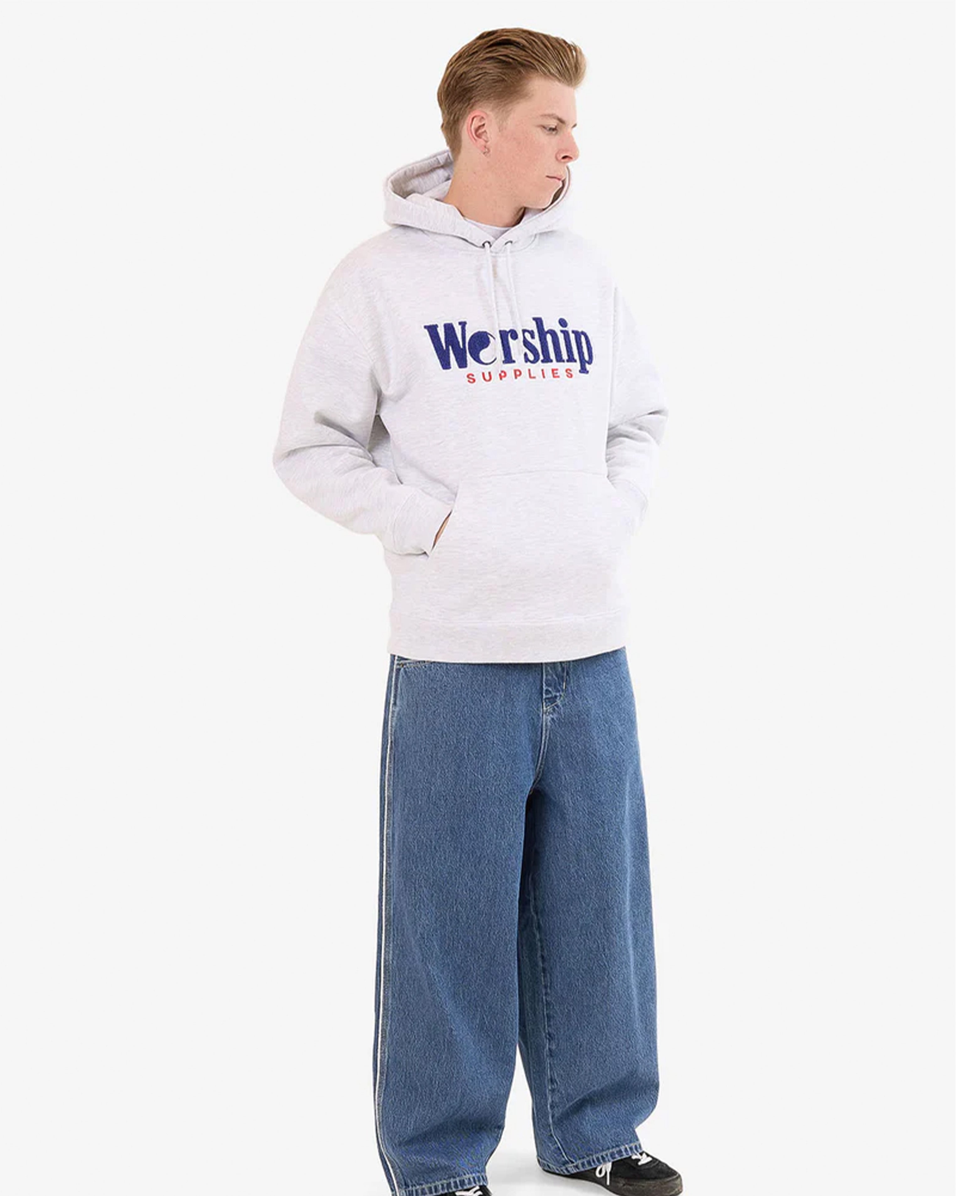 Full-body view of model in light grey Worship Supplies hoodie with wide-leg jeans and black sneakers