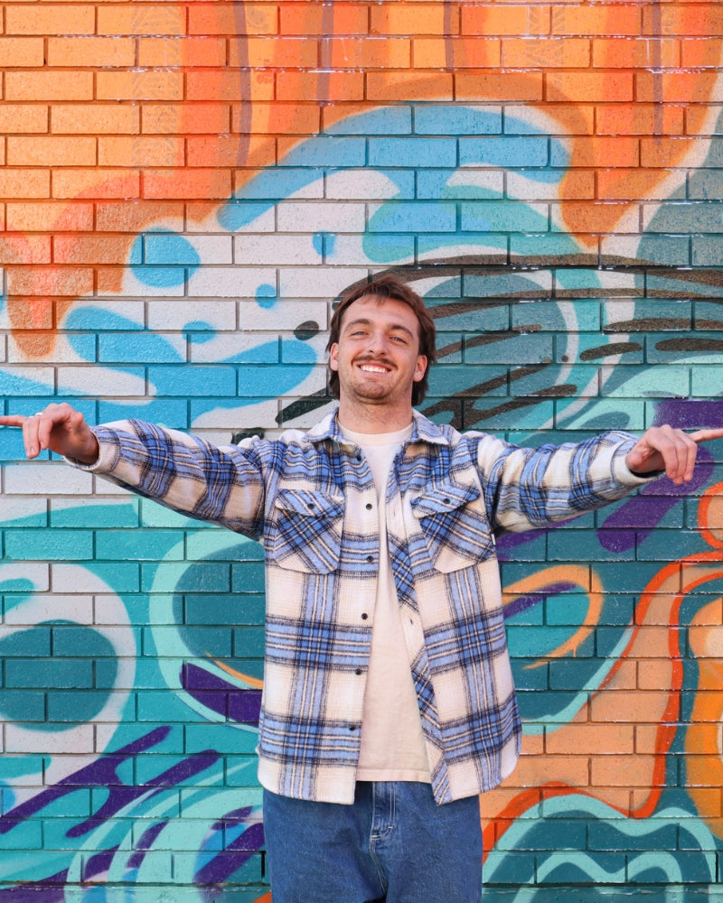 Person wearing a plaid shirt in front of a colorful mural.