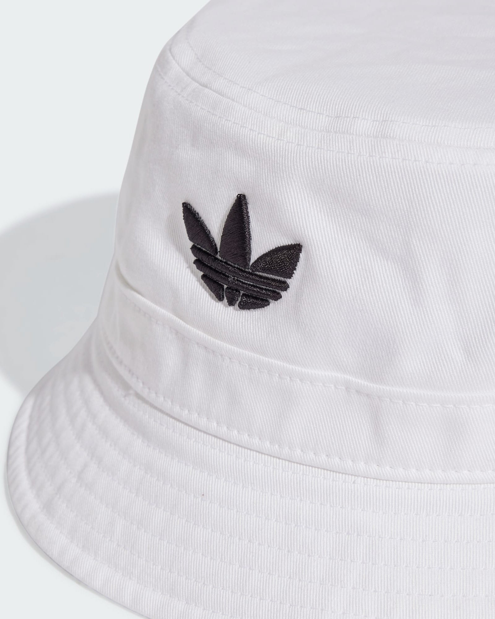 Close-up of white adidas bucket hat featuring stitched brim and black Trefoil logo detail on the crown.