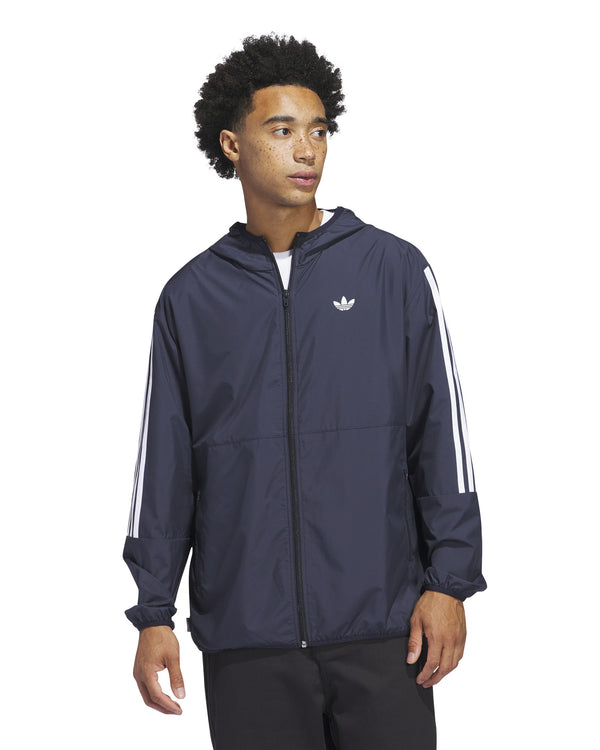 Man wearing a navy Adidas windbreaker jacket with white three-stripe detailing on the sleeves and a Trefoil logo on the chest.