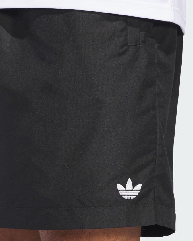 Close-up of Adidas Trefoil logo embroidered in white on the front hem of black shorts