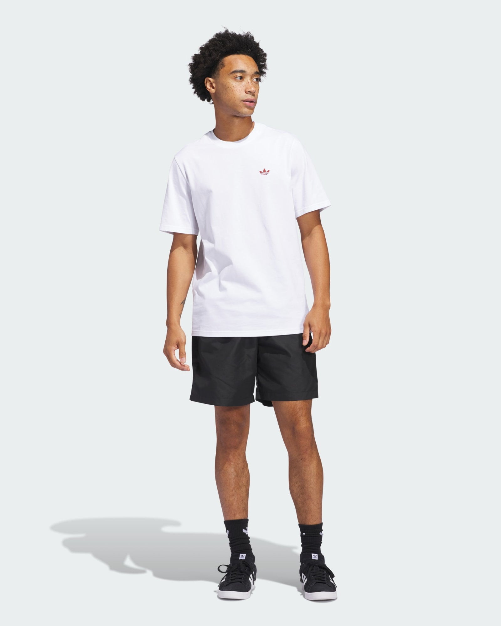 Man wearing black Adidas shorts, white tee and sneakers, styled for a casual streetwear look