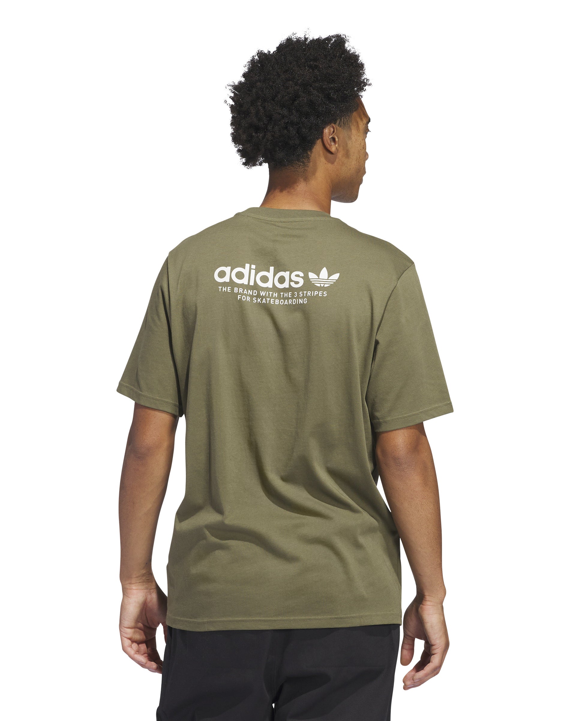 Back view of a model wearing an olive green Adidas t-shirt with white skateboarding logo text, paired with black pants.