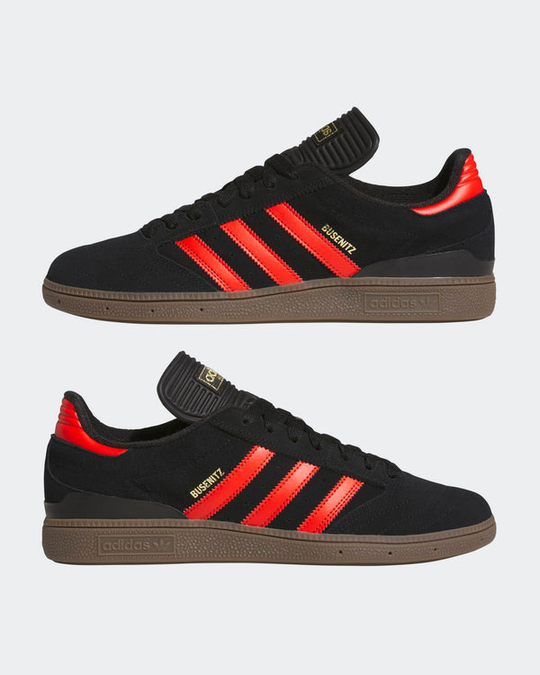 Pair of black Adidas sneakers with bright red stripes, gold branding, and gum soles, showcasing a sleek and sporty style.