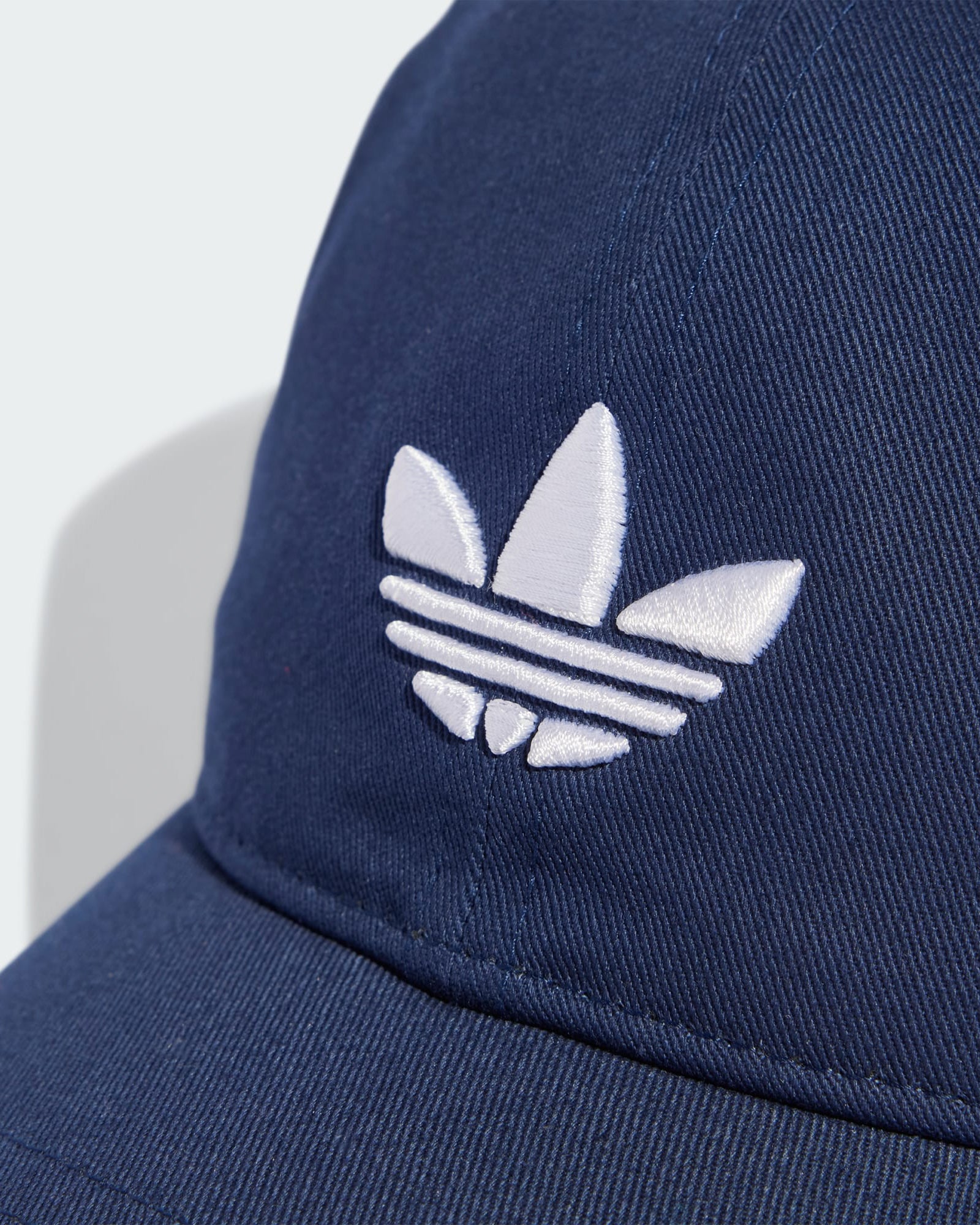 Close-up of Adidas Trefoil logo embroidery in white on navy cotton twill fabric