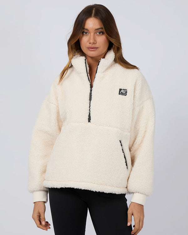 Model wearing a cozy cream sherpa fleece pullover with a half-zip front, black logo patch, and kangaroo pocket.